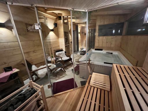 Wellnessbereich mit Sauna, Entspannungsstühlen und Whirlpool in warmem Holzambiente.