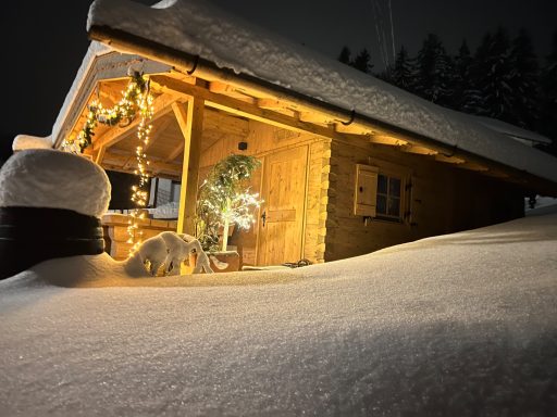 Holzhütte im Schnee, warm beleuchtet mit Weihnachtsdekor, umgeben von schneebedeckten Bäumen.